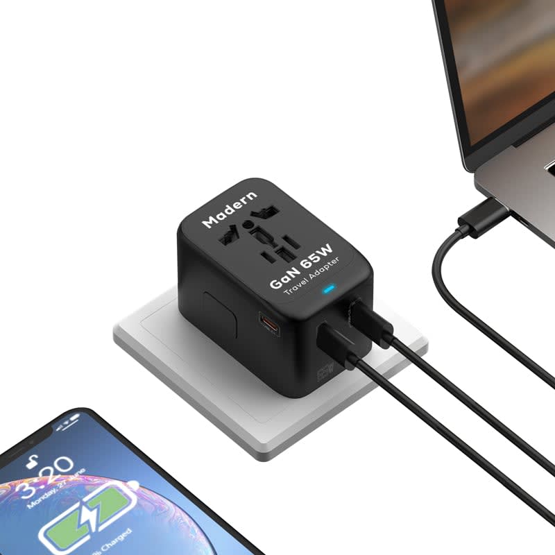 A black Madern 65W GaN PD and QC travel adaptor with multiple ports, connected to a laptop and a phone.