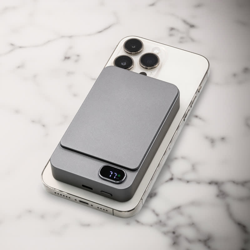 A grey magnetic wireless power bank rests on a smartphone, displaying a sleek and modern design against a marble background.