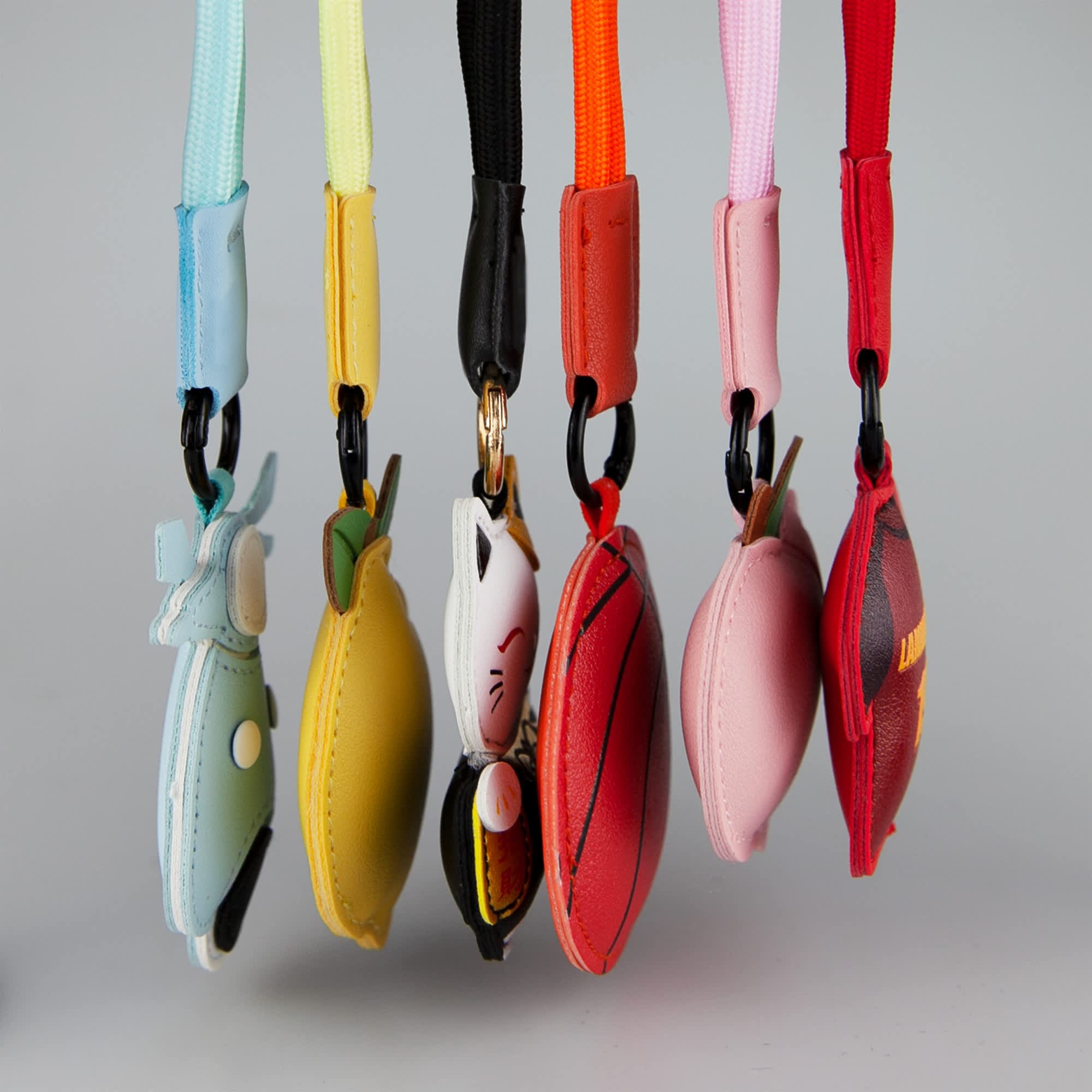 Five colourful bag charms hang from a display, featuring various designs like fruits and animals.