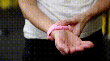 A pink wristband hand sanitiser dispenser on a person's wrist, designed for convenient sanitising.