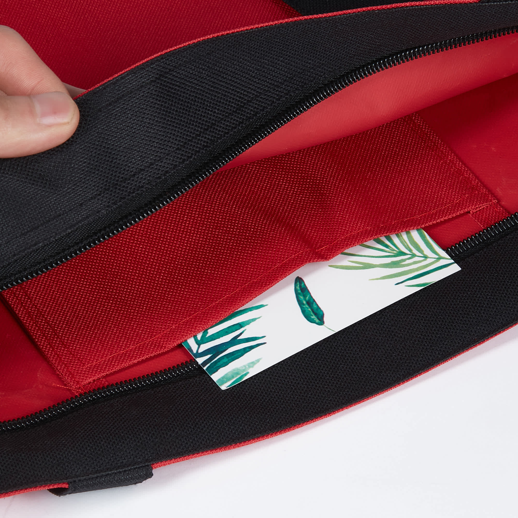 A red tote bag with a black trim, featuring an interior pocket and a decorative card inside.
