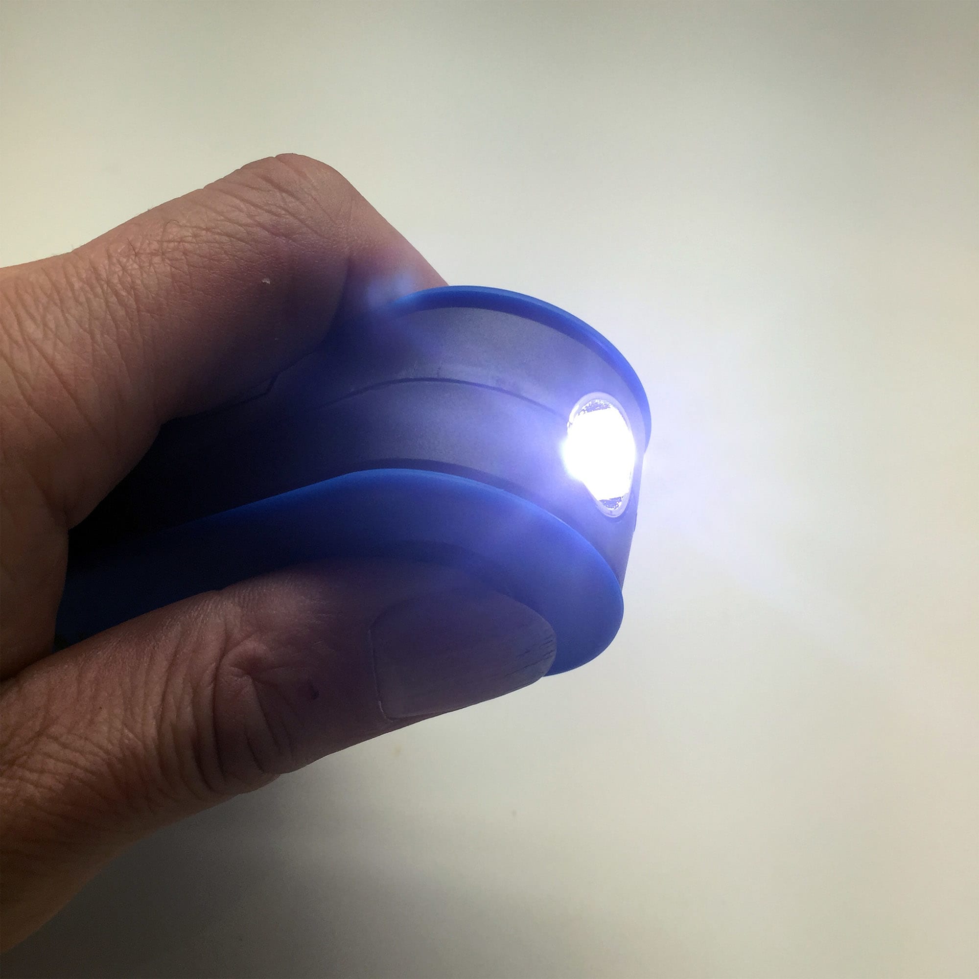A blue 360 Degree Torch held in a hand, emitting a bright light from its front end.