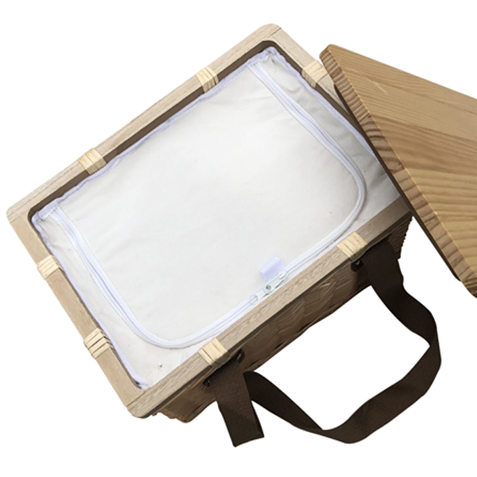 A square wicker picnic cooler basket with a light-coloured interior and brown straps, partially open.