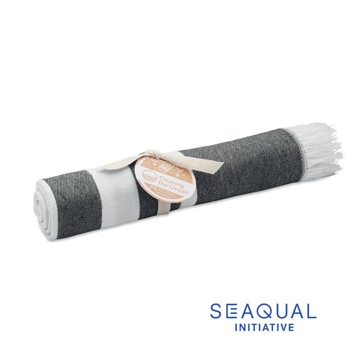 A rolled-up grey beach towel with fringe detailing, tied with a string label. The image includes a logo.