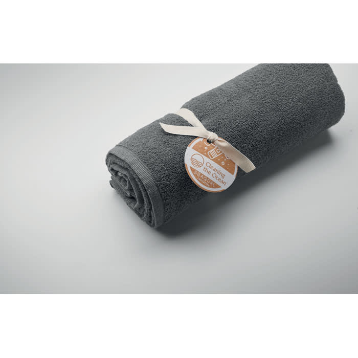 A rolled grey towel tied with a ribbon, featuring a tag with a logo.