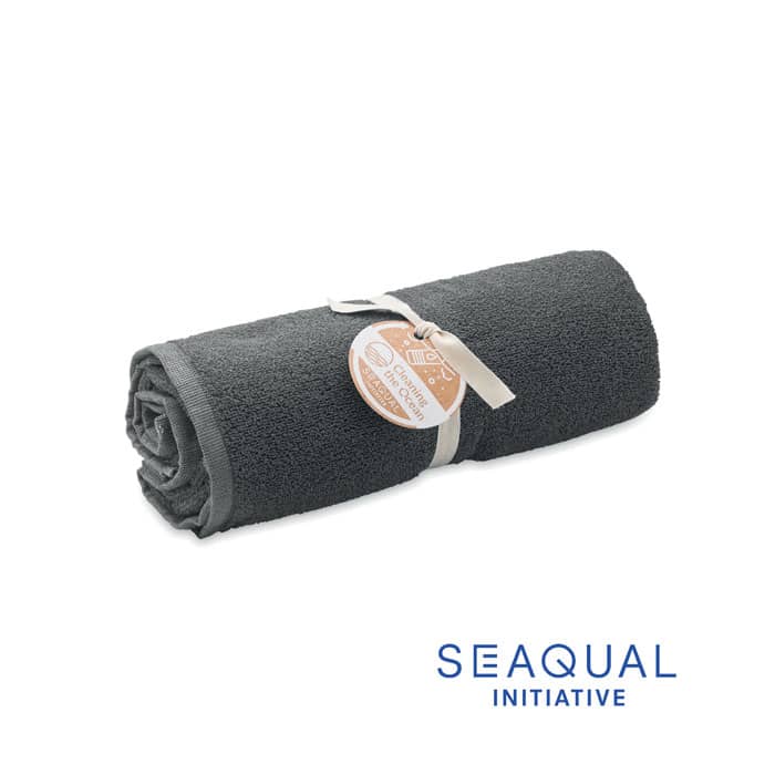 A rolled grey towel tied with a ribbon, featuring a tag. It includes a logo at the bottom right.