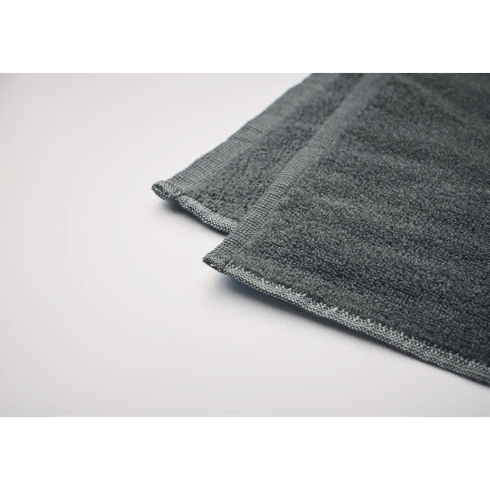 A grey towel folded neatly with a textured surface, featuring a simple stitch along the edges.