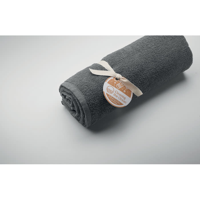 A rolled grey towel wrapped with a ribbon and a tag, resting on a light grey surface.