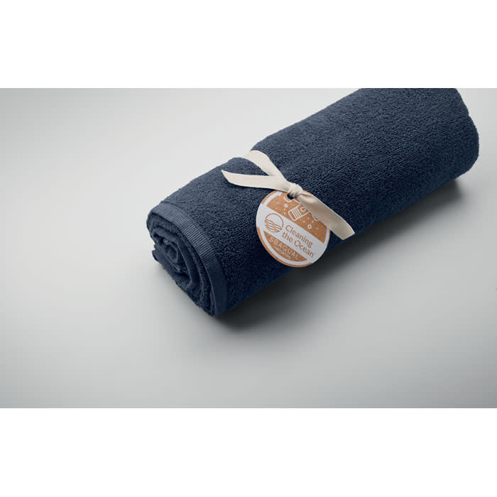 A rolled navy towel tied with a ribbon, featuring a tag with a logo and text.