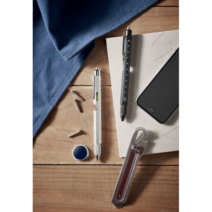 A collection of pens, a smartphone, screws, and a red liquid-filled tool on a wooden surface with a blue cloth.
