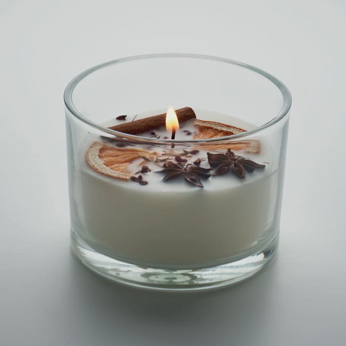 A glass candle featuring a white wax interior, topped with dried orange, cinnamon stick, and star anise.