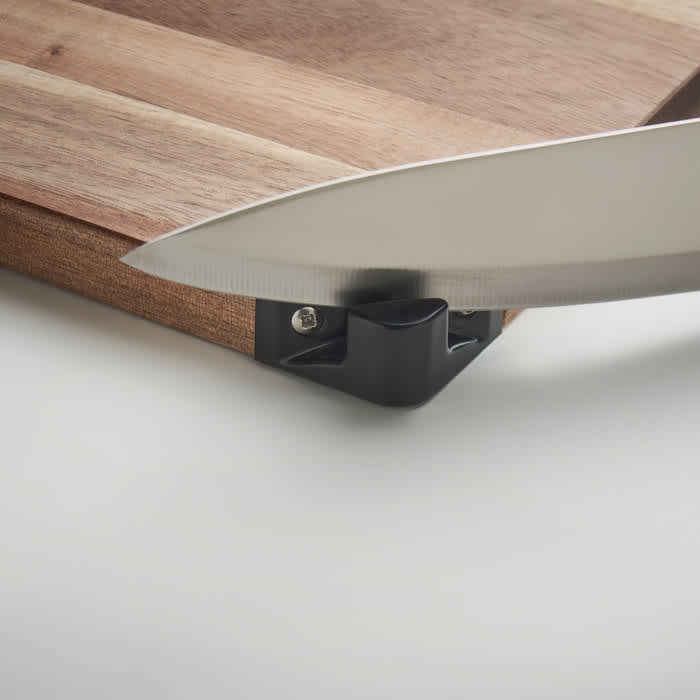 A cutting board with a wooden surface and a black corner piece, featuring a metal knife poised above it.