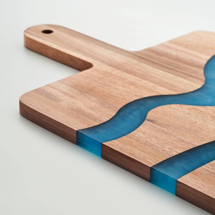 A cutting board featuring a natural wood finish with a blue resin river design. It has a handle and a unique shape.