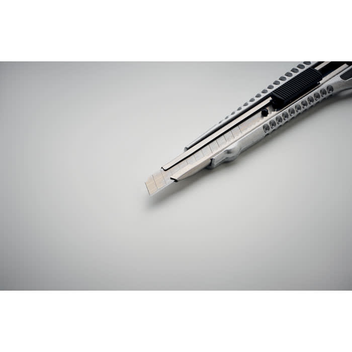 A utility knife featuring a metallic finish, with a retractable blade and sleek design, placed on a grey surface.