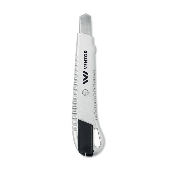 A metallic utility knife with a serrated edge and a black rubber handle, featuring a logo.