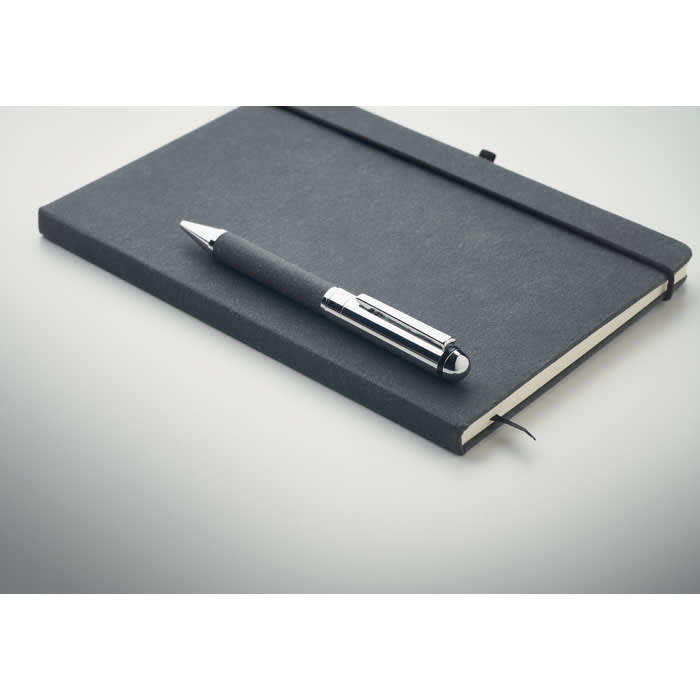 A black notebook and a sleek black pen are arranged on a light surface. The notebook has a logo on the cover.