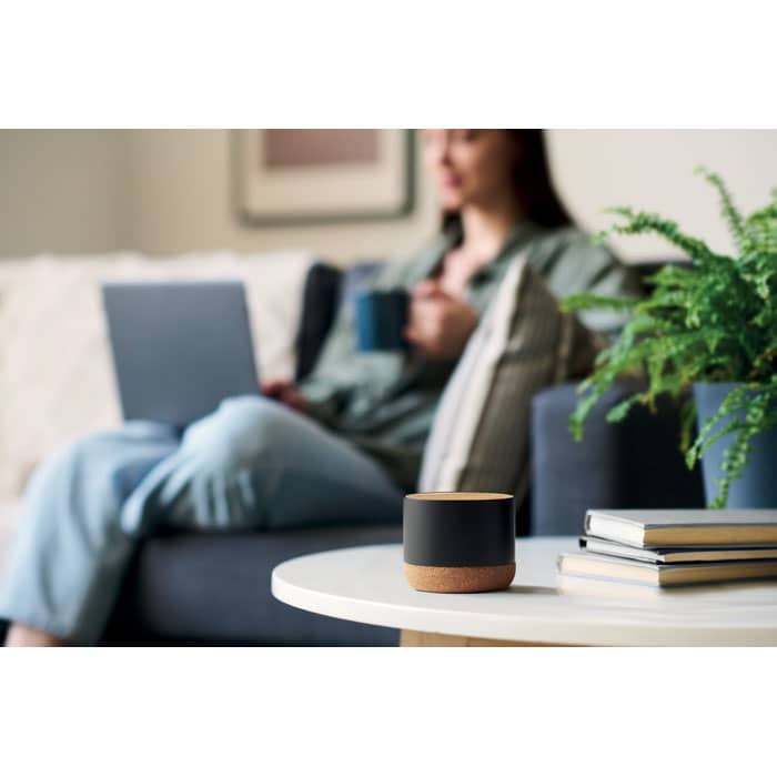 A drink bottle in black with a wooden base sits on a table next to books, with a blurred person in the background.