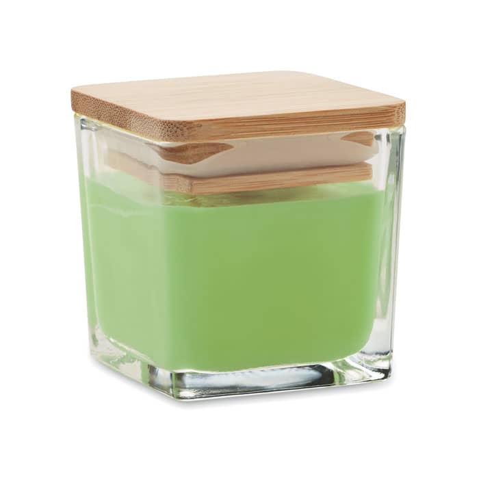 A square glass container with a green candle inside and a wooden lid. The design is sleek and modern.