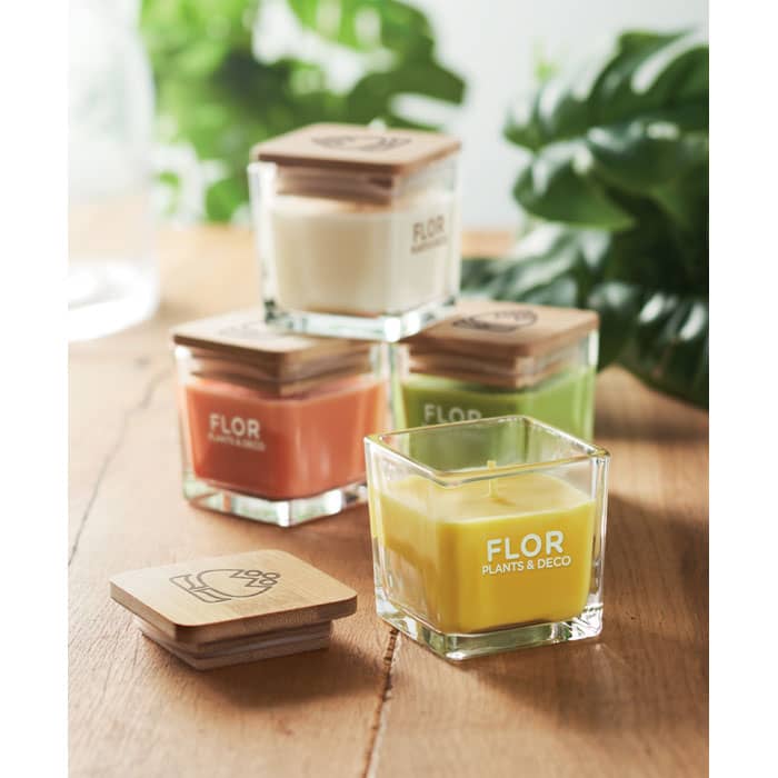 A set of four glass candles in various colours, each with a wooden lid and a branded logo.