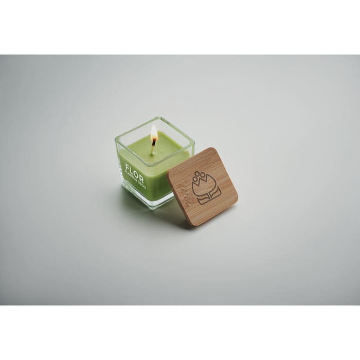A green candle in a glass container with a wooden lid, featuring a simple logo design.