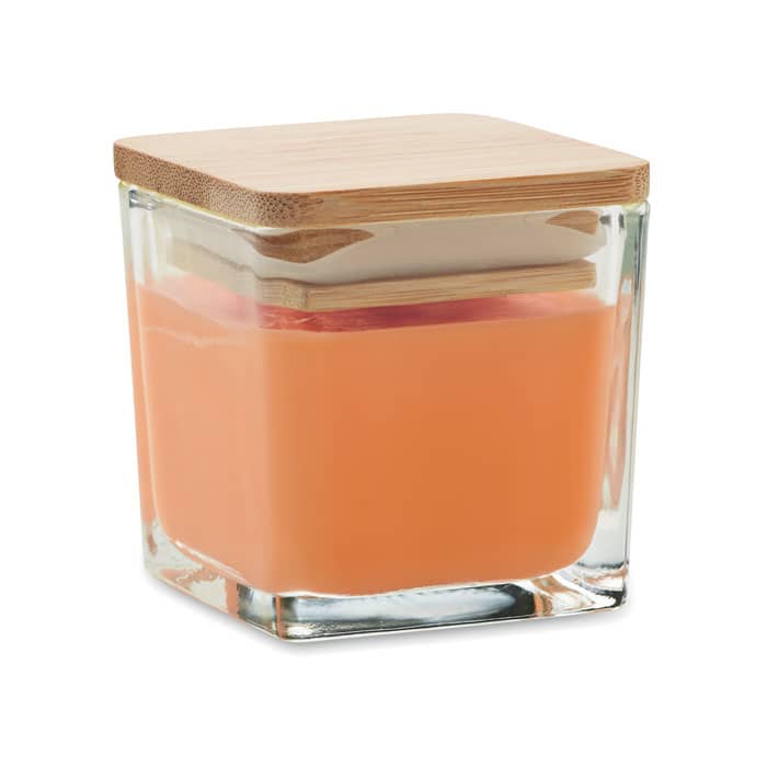 A glass container with a square shape, filled with peach-coloured liquid and a wooden lid on top.