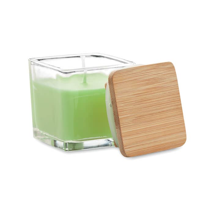 A green candle in a glass container with a square bamboo lid beside it.