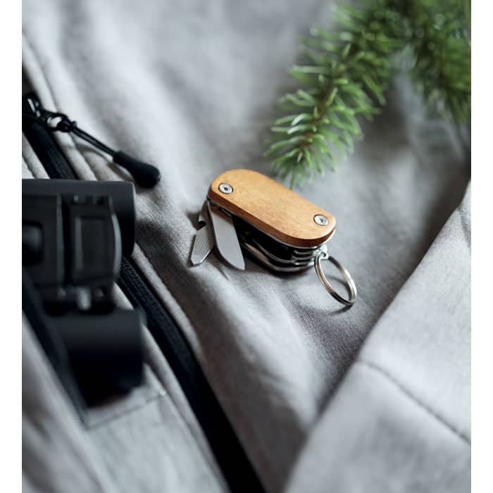 A compact multi-tool with a wooden handle and metal blades, resting on a grey fabric surface.