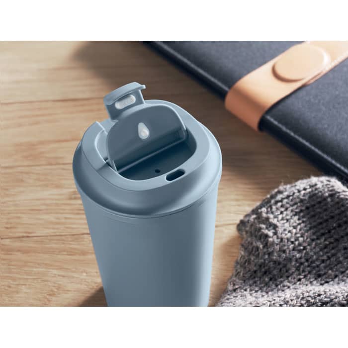 A drink bottle in light blue with a flip-top lid, placed on a wooden surface beside a notebook and a knitted item.