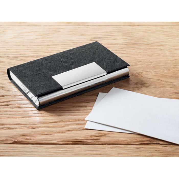 A black business card holder with a silver clasp, accompanied by two blank white cards, on a wooden surface.