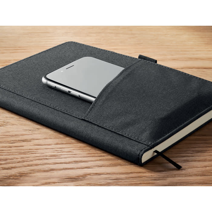 A black notebook with a pocket, featuring a smartphone resting in the pocket, placed on a wooden surface.