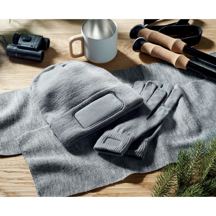 A drink bottle with a grey knitted beanie, gloves, and a grey scarf on a wooden surface.