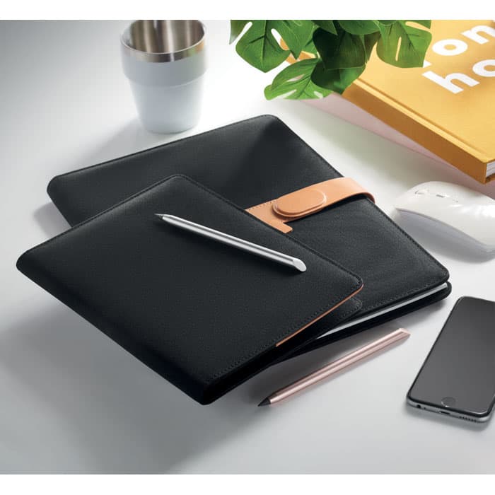 A black faux leather folder and notebook set, accompanied by a silver pen, smartphone, and a plant.