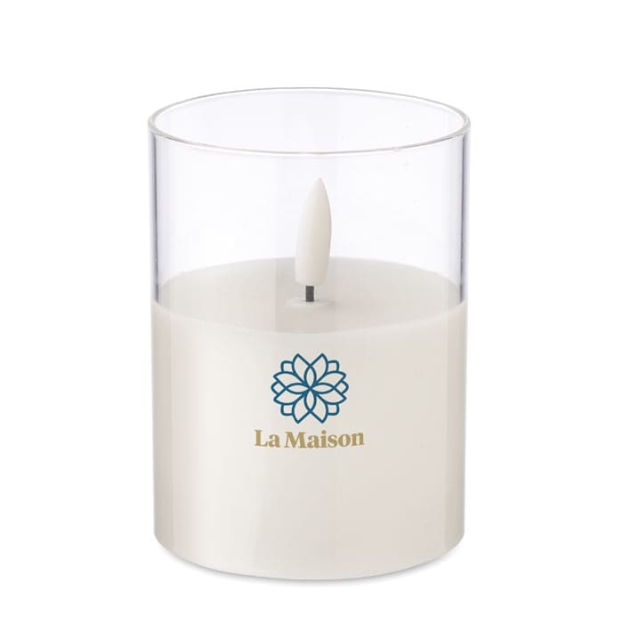 A candle in a transparent glass holder featuring a white wax centre and a floral logo.