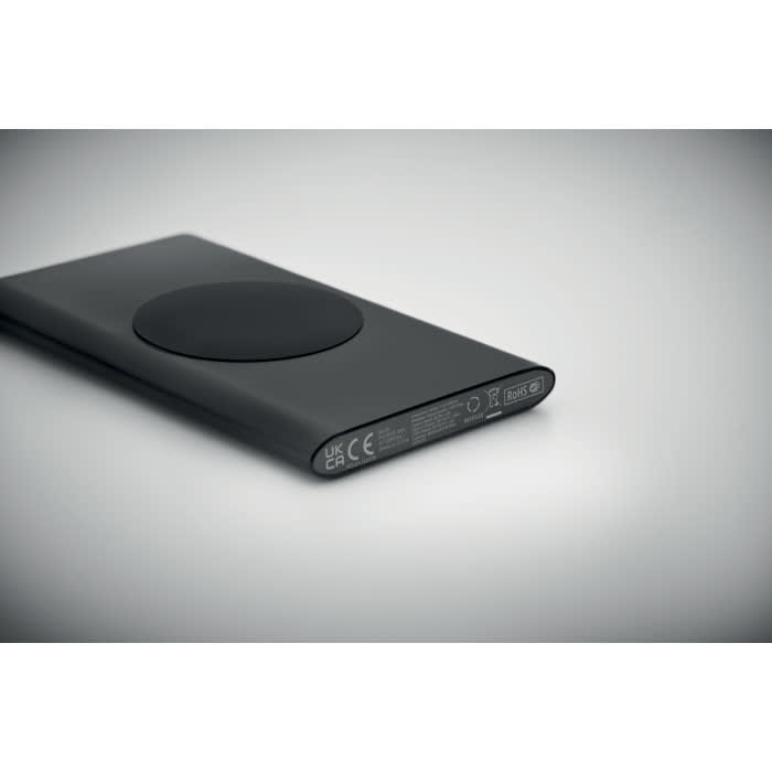 A sleek black power bank with a circular charging pad on one side, featuring various technical details on the bottom edge.