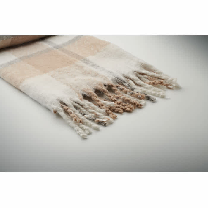 A throw blanket in soft beige and white plaid pattern, featuring fringed edges for added texture.