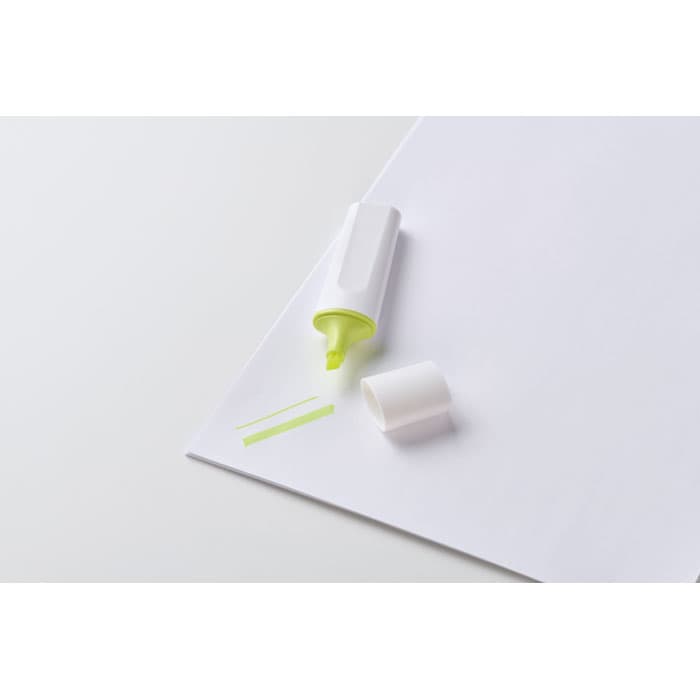 A highlighter in white and neon green on a blank sheet of paper, with a cap removed and a small strip nearby.