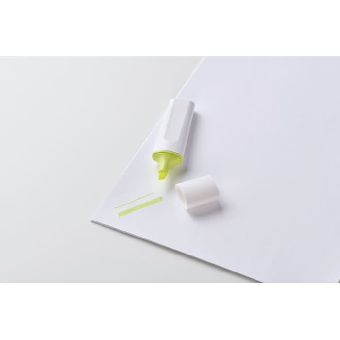 A highlighter in white casing with a bright green tip sits on a blank piece of paper, with a few lines drawn next to it.