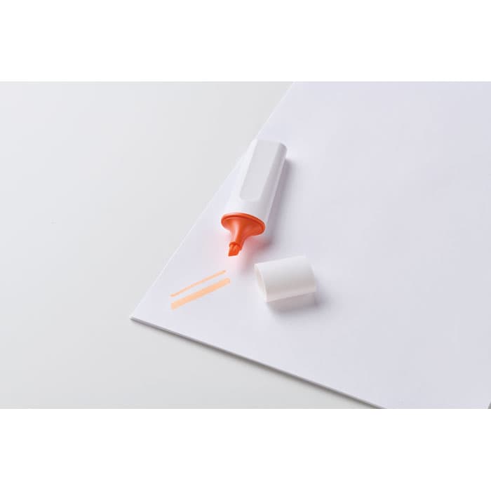 A highlighter in orange colour, lying on a white sheet of paper, with the cap beside it.