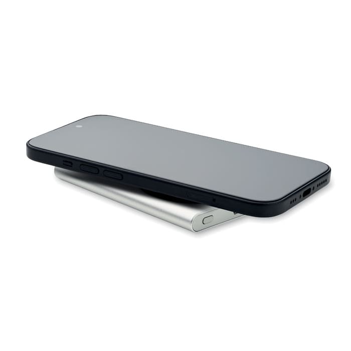A smartphone in black rests on a silver charging pad, showcasing a sleek design. The image features a logo.