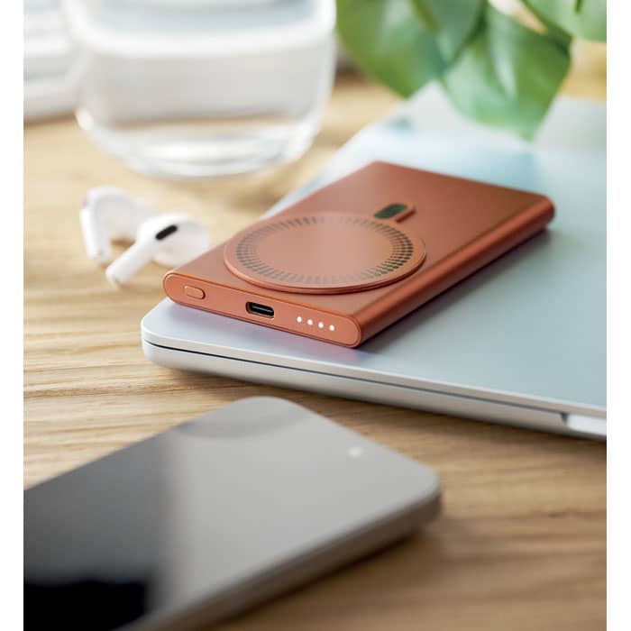 A drink bottle in a metallic copper hue, featuring a logo, placed on a wooden surface alongside electronic devices.