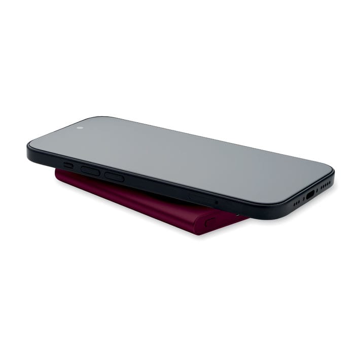 A sleek black smartphone resting on a burgundy charging pad, showcasing a minimalist design.