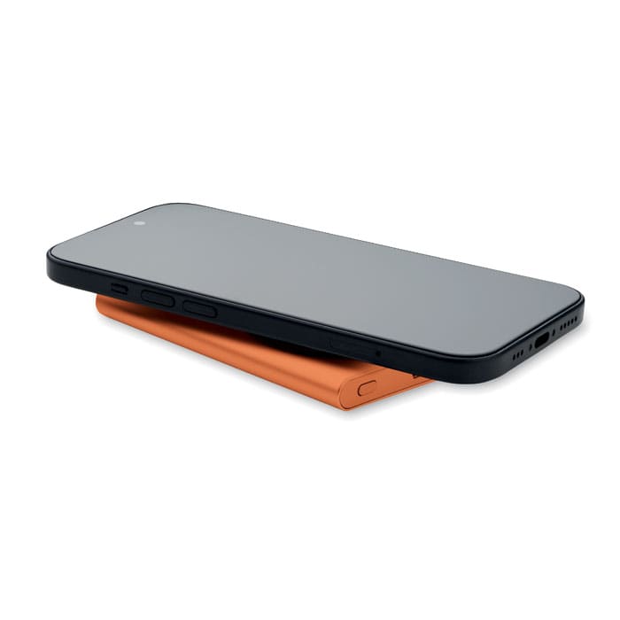 A smartphone in black resting on an orange charging pad, featuring a sleek design and a minimalist look.