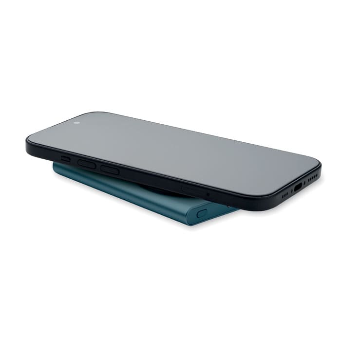 A smartphone rests on a teal wireless charging pad. The pad is slim and features rounded edges.