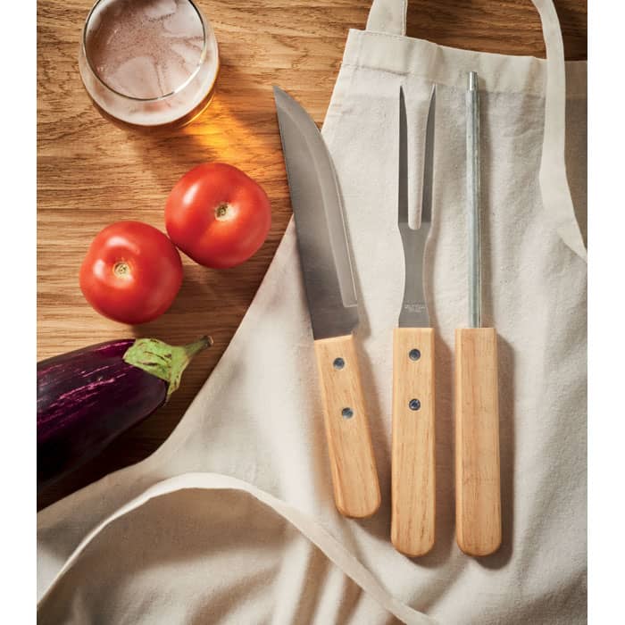 A collection of three kitchen knives with wooden handles, alongside two tomatoes and an eggplant on a cloth surface.