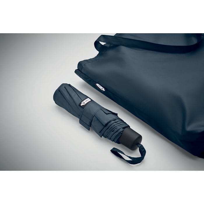A navy umbrella beside a matching tote bag, both designed with sleek and modern styling. The umbrella is folded and compact.