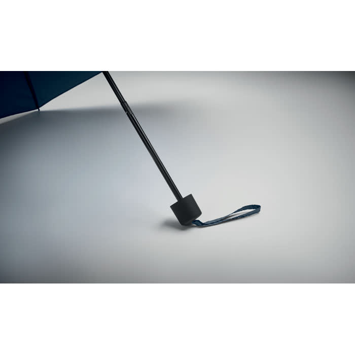 A blue umbrella with a black handle sits on a light grey surface, featuring a strap attached to the handle.