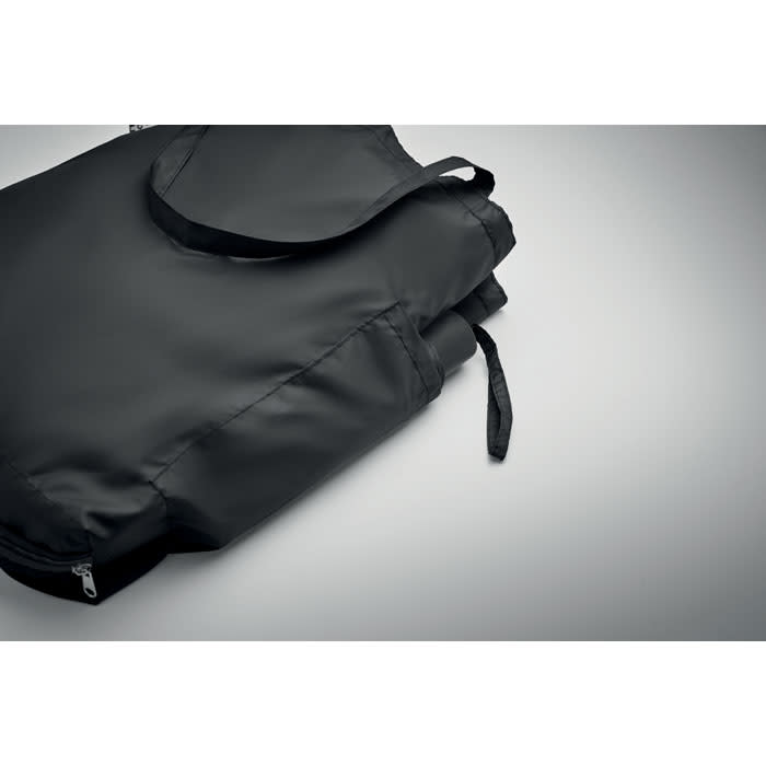 A black foldable bag with a strap, displayed on a grey background. The bag is zipped and partially rolled.