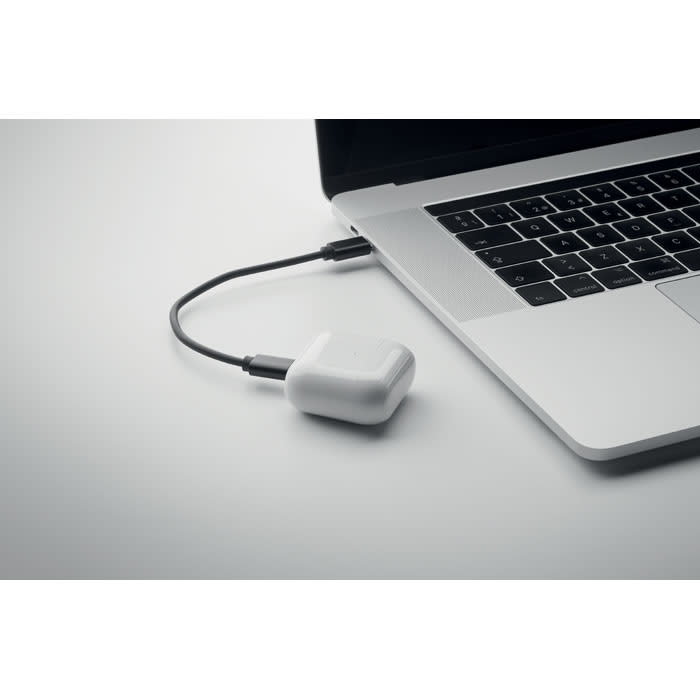 A charging device in white connected to a laptop via a black cable, placed on a light grey surface.