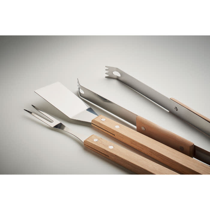 A set of stainless steel grilling tools including a spatula, fork, tongs, and a grill brush with wooden handles.