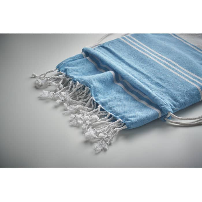 A blue drawstring bag with white stripes and fringes, featuring a soft fabric texture. It has a simple logo.